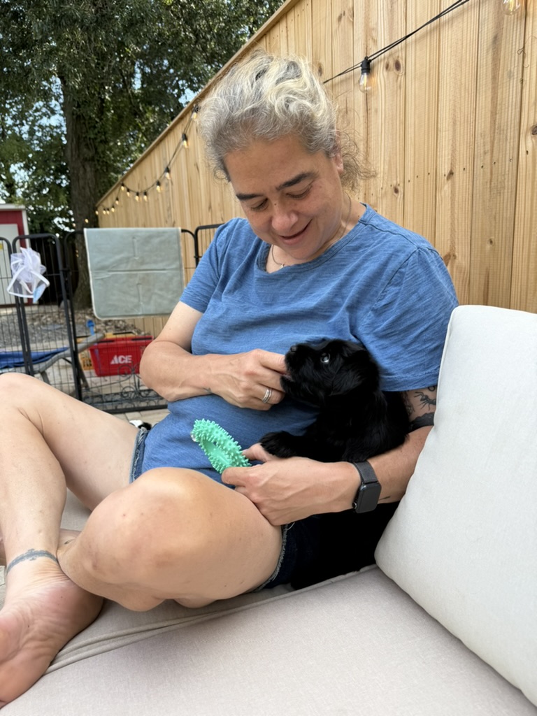 Deidre cuddling a puppy with a textured chew toy on a patio